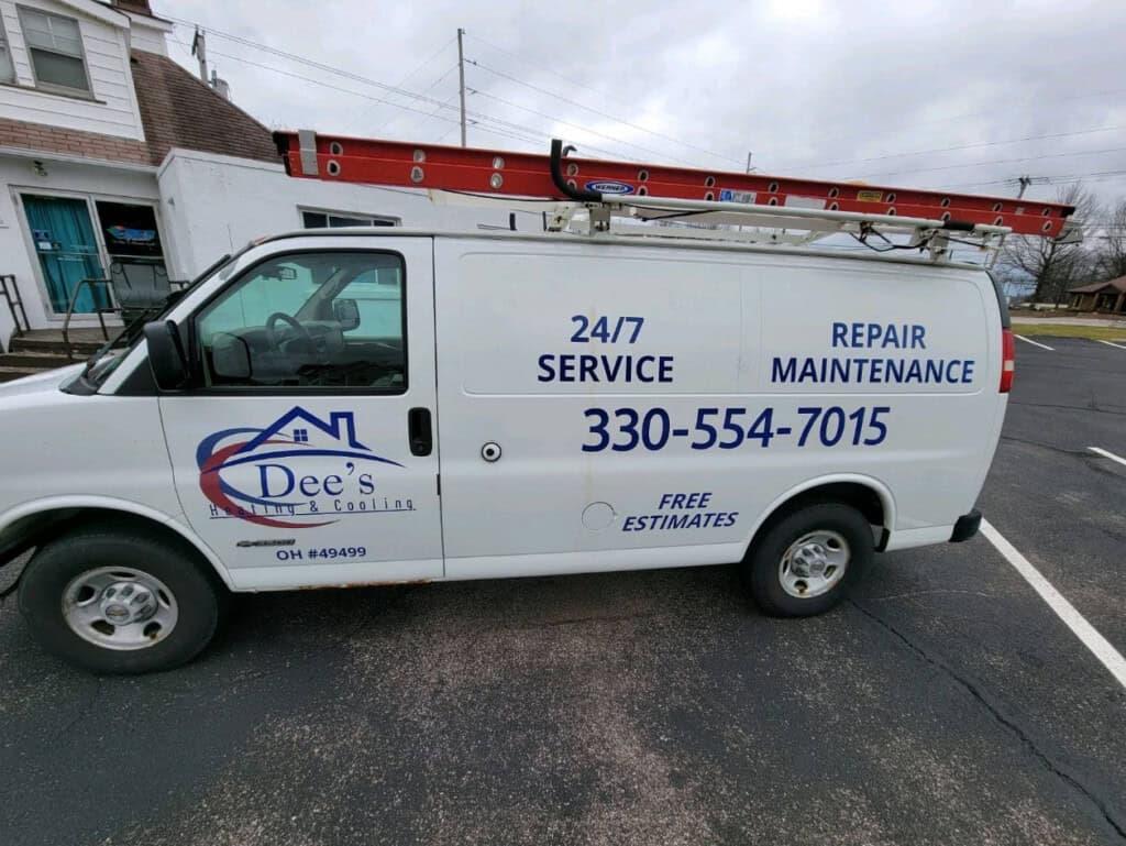 A white van with Dee’s Plumbing & Cooling logo, contact number 330-554-7015, and text for 24/7 service, repair, and maintenance. A ladder is secured on top and the van is parked in a lot near buildings.