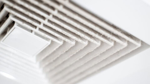 Close-up of a white ceiling air vent covered in dust, showing the accumulation on the vent slats.