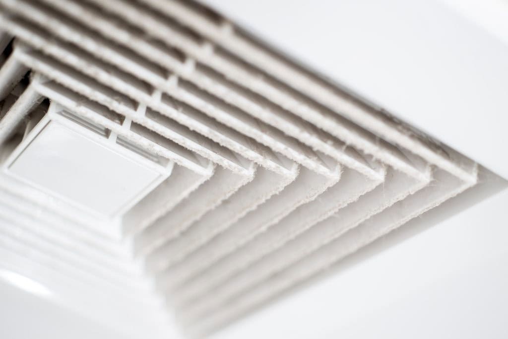 Close-up of a white ceiling air vent covered in dust, showing the accumulation on the vent slats.