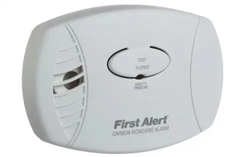 A white First Alert carbon monoxide alarm with a central test/silence button and vent openings on the left side. “First Alert Carbon Monoxide Alarm” is printed on the lower front of the device.
