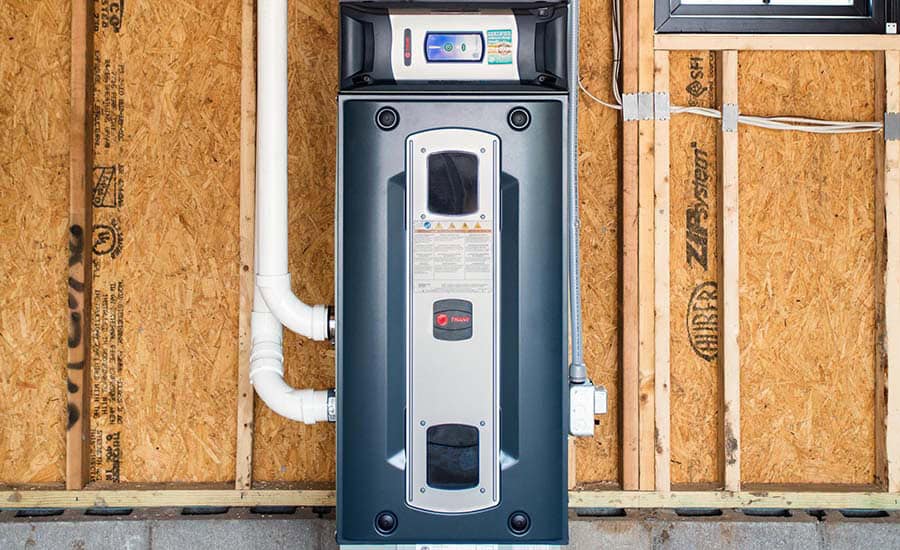 A modern gray water heater installed on an unfinished wall with exposed wooden studs and insulation, along with visible pipes and an electrical outlet nearby.